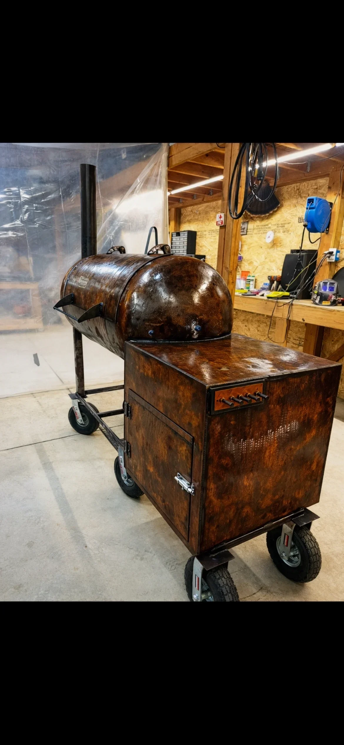 Welded steel barrel smoker with cooking chamber on wheeled cart in workshop